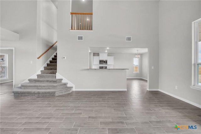unfurnished living room with stairway, a high ceiling, visible vents, and baseboards