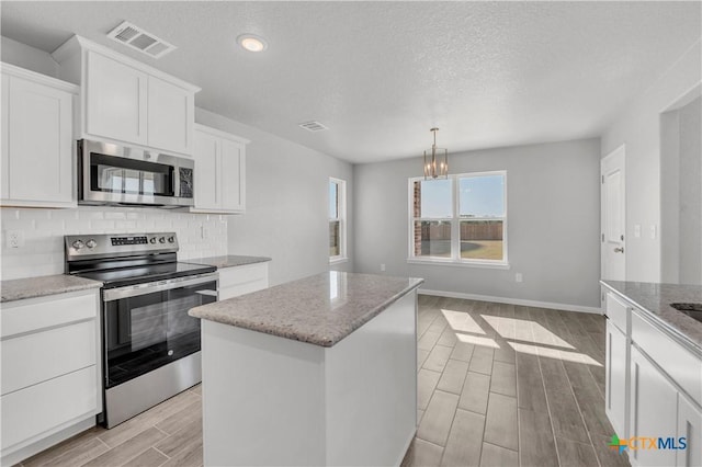 kitchen featuring wood tiled floor, stainless steel appliances, visible vents, a center island, and tasteful backsplash