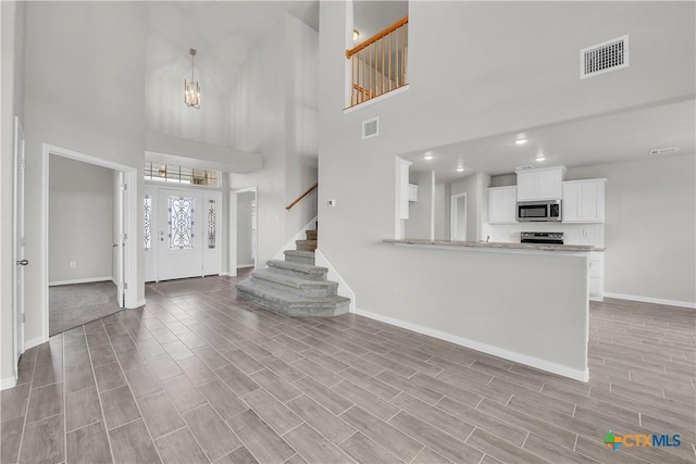 foyer with visible vents, baseboards, stairs, and a high ceiling