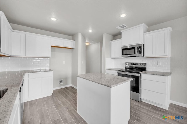 kitchen with baseboards, visible vents, a kitchen island, and appliances with stainless steel finishes