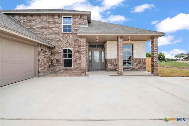 view of front of property featuring an attached garage, brick siding, and roof with shingles