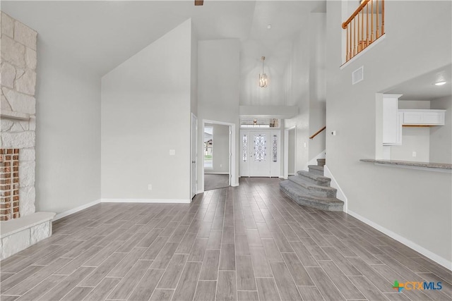 unfurnished living room featuring baseboards, a towering ceiling, an inviting chandelier, and stairway