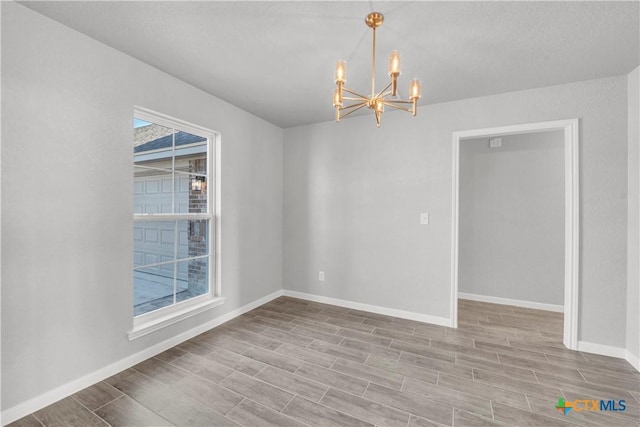 spare room with wood finished floors, baseboards, and a notable chandelier