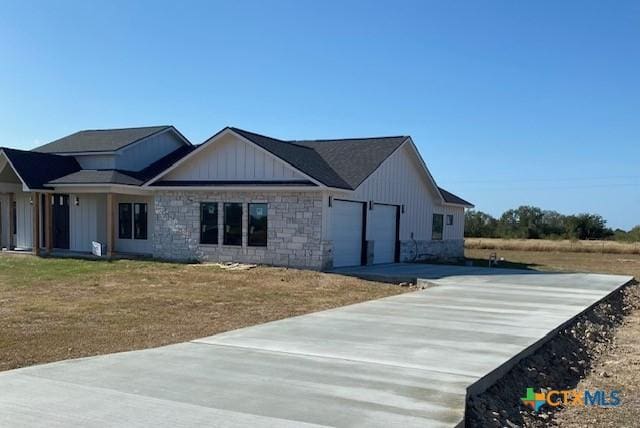 view of front of property with an attached garage, concrete driveway, stone siding, a front lawn, and board and batten siding