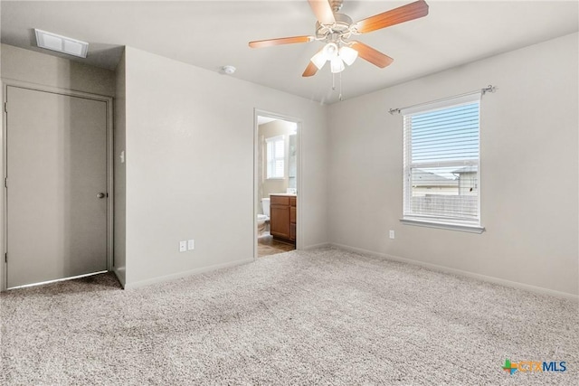 unfurnished bedroom featuring multiple windows, ceiling fan, carpet flooring, and ensuite bath