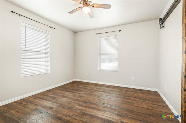 spare room featuring dark wood-type flooring, a barn door, ceiling fan, and plenty of natural light