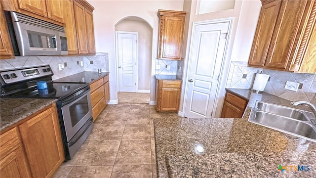 kitchen with sink, appliances with stainless steel finishes, dark stone countertops, tile patterned floors, and decorative backsplash