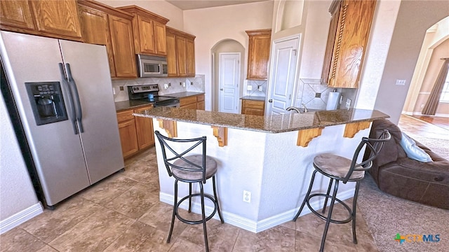 kitchen featuring stainless steel appliances, a breakfast bar area, dark stone counters, and backsplash