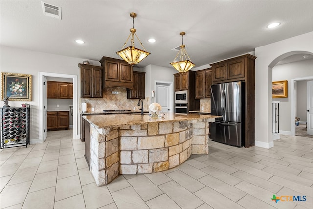 kitchen with pendant lighting, decorative backsplash, stainless steel appliances, and a center island with sink