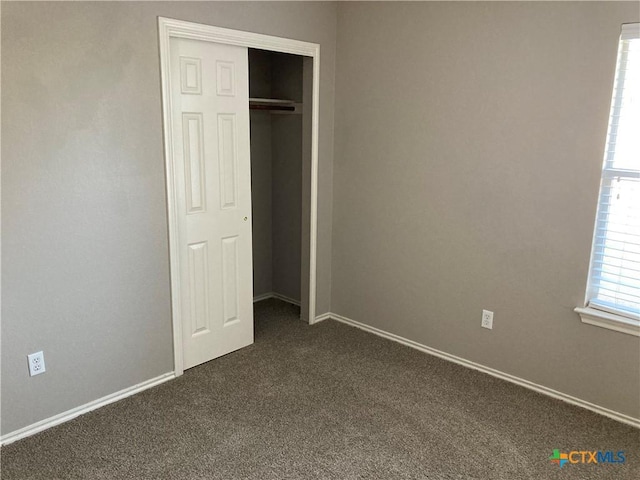 unfurnished bedroom with dark colored carpet and a closet