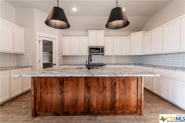 kitchen with white cabinets, a kitchen island with sink, and decorative light fixtures