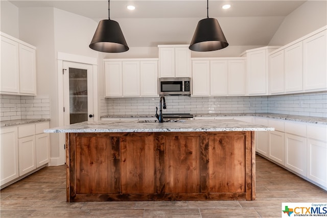 kitchen with light stone counters, hanging light fixtures, and an island with sink