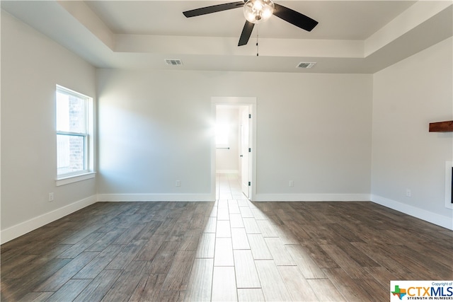 spare room featuring dark wood-type flooring, ceiling fan, and a raised ceiling