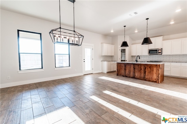 kitchen with white cabinetry, pendant lighting, an island with sink, and backsplash