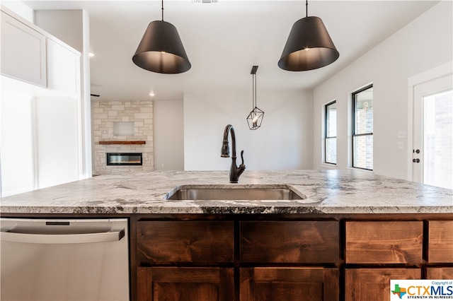 kitchen featuring a stone fireplace, sink, stainless steel dishwasher, light stone countertops, and pendant lighting