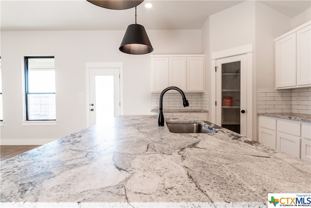 kitchen with white cabinetry, decorative backsplash, sink, and light stone counters