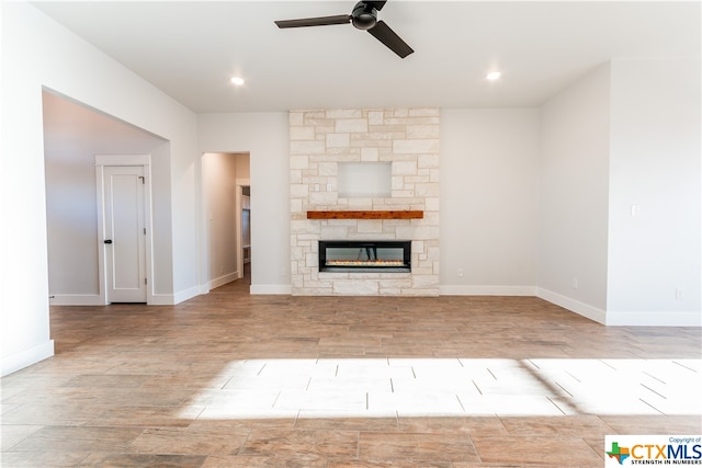 unfurnished living room featuring a stone fireplace, light hardwood / wood-style floors, and ceiling fan