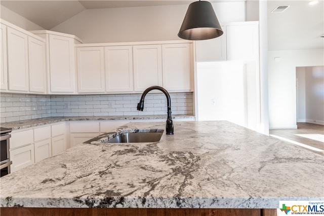 kitchen featuring an island with sink, vaulted ceiling, light stone countertops, and decorative backsplash