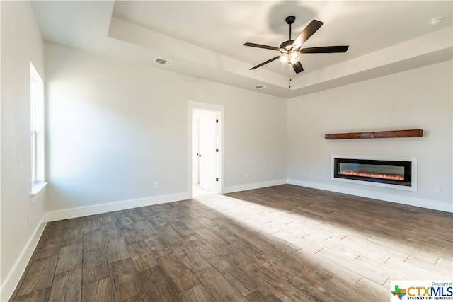 unfurnished living room with hardwood / wood-style flooring, ceiling fan, and a raised ceiling