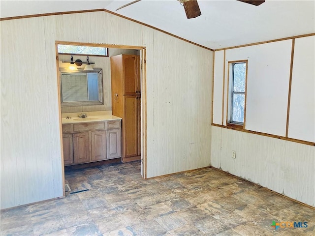 empty room with a sink, wooden walls, ceiling fan, lofted ceiling, and ornamental molding