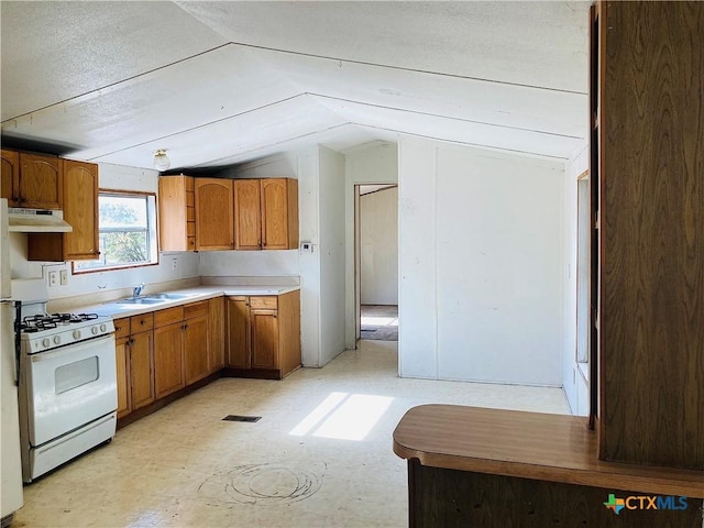 kitchen with brown cabinetry, lofted ceiling, under cabinet range hood, and white range with gas cooktop