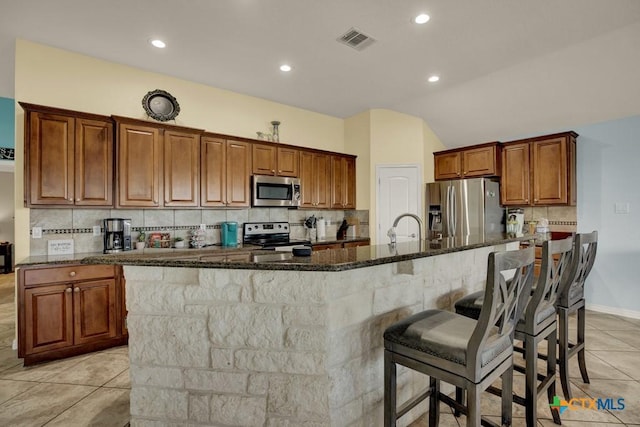 kitchen with stainless steel appliances, dark stone countertops, a spacious island, visible vents, and backsplash
