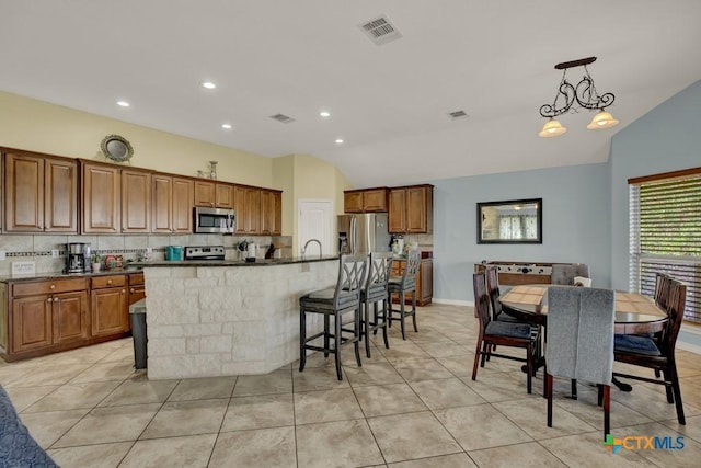 kitchen featuring lofted ceiling, a large island, visible vents, brown cabinetry, and appliances with stainless steel finishes