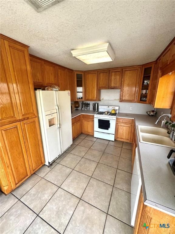 kitchen featuring sink, white appliances, a textured ceiling, and light tile patterned flooring