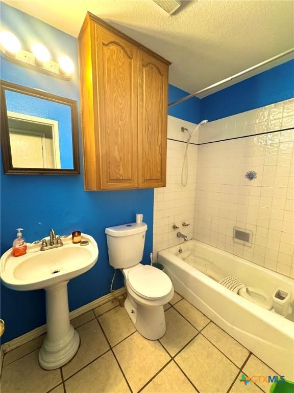 bathroom with tiled shower / bath combo, tile patterned floors, toilet, and a textured ceiling