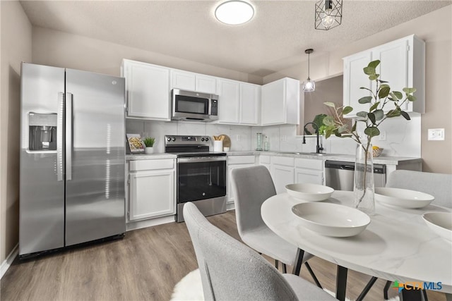 kitchen with sink, appliances with stainless steel finishes, decorative backsplash, white cabinets, and decorative light fixtures