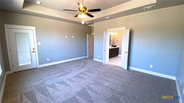 unfurnished bedroom featuring ensuite bath, sink, ceiling fan, a tray ceiling, and light colored carpet