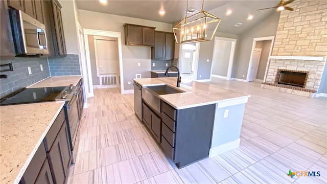 kitchen featuring vaulted ceiling, sink, light stone countertops, appliances with stainless steel finishes, and decorative light fixtures