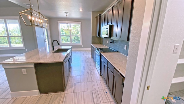 kitchen with stainless steel appliances, hanging light fixtures, sink, a kitchen island with sink, and light stone countertops