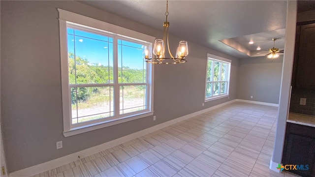 unfurnished dining area featuring a raised ceiling and ceiling fan with notable chandelier