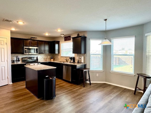 kitchen with appliances with stainless steel finishes, tasteful backsplash, hanging light fixtures, a center island, and dark hardwood / wood-style flooring