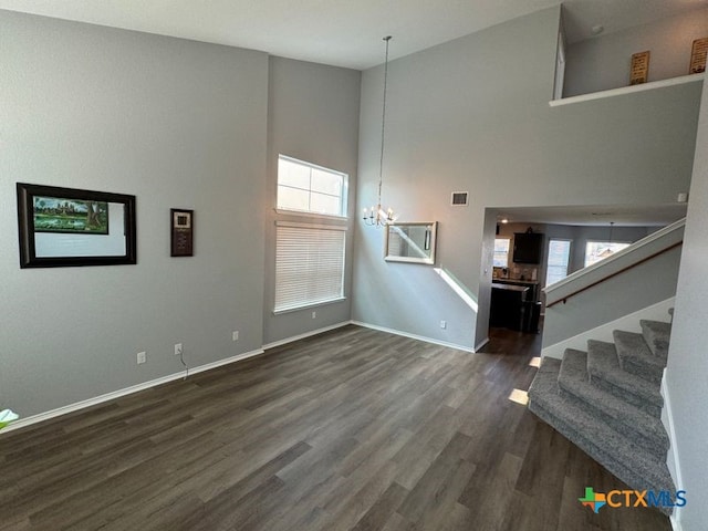 unfurnished living room featuring dark wood-type flooring, a high ceiling, and a notable chandelier