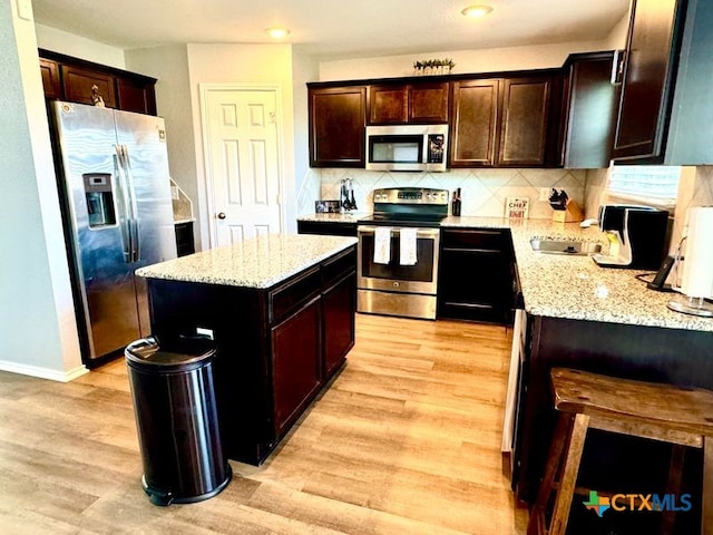 kitchen featuring stainless steel appliances, light hardwood / wood-style flooring, light stone counters, and a center island