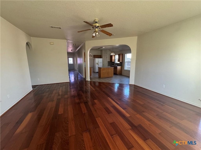 unfurnished living room with ceiling fan, dark wood-type flooring, and a textured ceiling