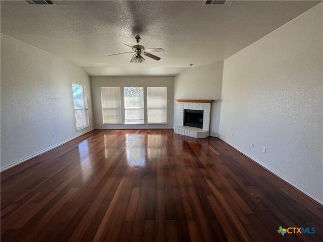 unfurnished living room featuring ceiling fan, dark hardwood / wood-style flooring, a textured ceiling, and a brick fireplace