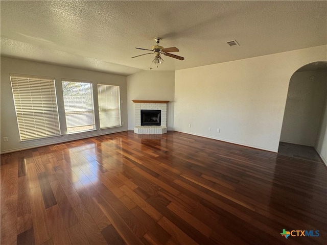 unfurnished living room with ceiling fan, a fireplace, dark hardwood / wood-style flooring, and a textured ceiling