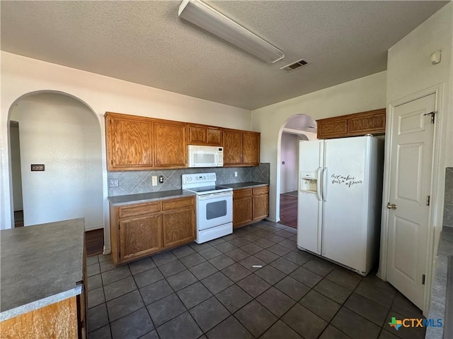 kitchen with decorative backsplash, a textured ceiling, white appliances, and dark tile patterned flooring