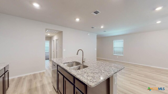 kitchen with dishwasher, sink, light stone counters, an island with sink, and light hardwood / wood-style floors