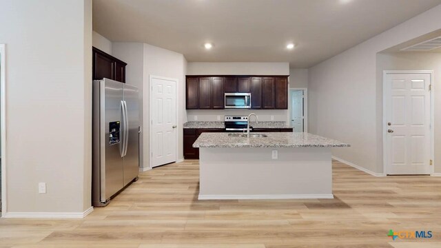 kitchen featuring light stone countertops, sink, stainless steel appliances, an island with sink, and light hardwood / wood-style floors