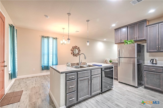 kitchen featuring pendant lighting, black dishwasher, an island with sink, sink, and stainless steel fridge