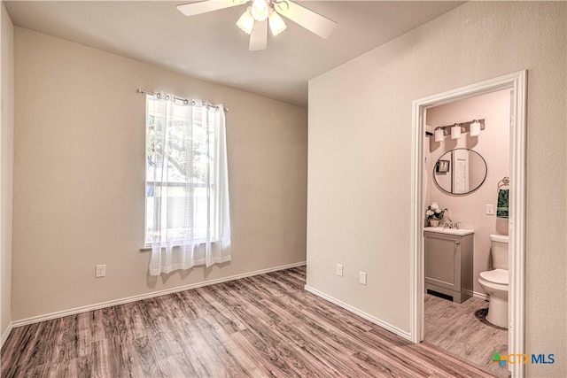 unfurnished bedroom featuring ensuite bath, ceiling fan, sink, and hardwood / wood-style flooring