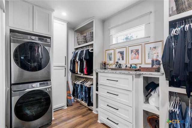 laundry area with cabinets, stacked washer and clothes dryer, and light wood-type flooring