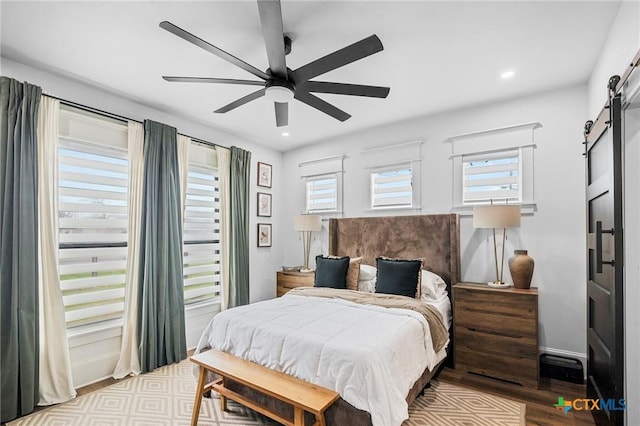 bedroom with ceiling fan, a barn door, and light wood-type flooring