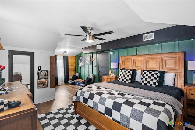 bedroom featuring vaulted ceiling, dark hardwood / wood-style floors, ceiling fan, and wood walls