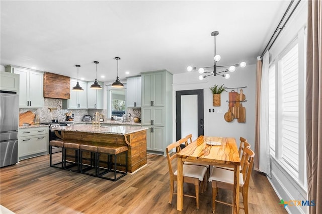 kitchen featuring an island with sink, a kitchen breakfast bar, hanging light fixtures, light stone counters, and stainless steel appliances