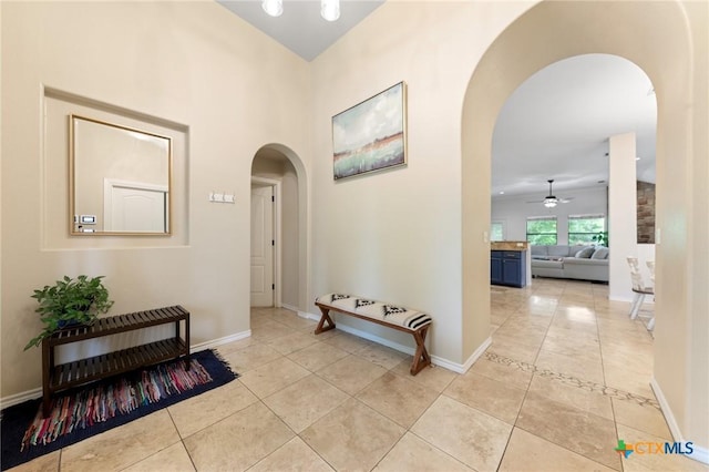 corridor featuring arched walkways, baseboards, and light tile patterned flooring